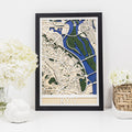 3D wooden city map of Kyiv with blue and green geometric details in a black frame hanging on a wall.