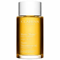 A clear glass bottle of golden amber Tonic Body-Firming Treatment Oil with white labeling.