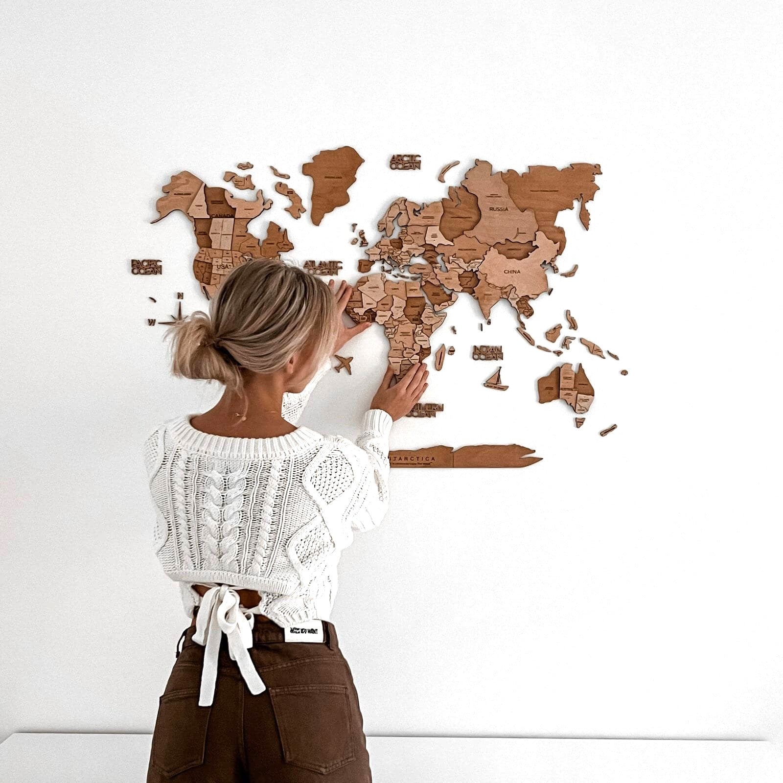 3D wooden world map in natural oak brown and tan tones displayed on a modern living room wall.