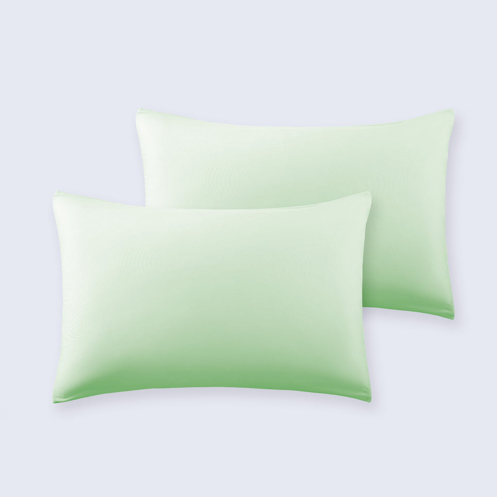 A pair of light green cooling pillowcases displayed on a clean white bed sheet.
