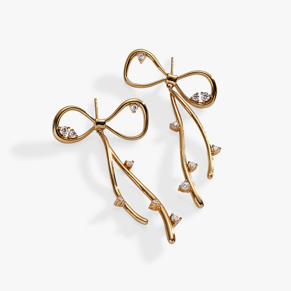 A pair of gold-finished coquette bow earrings with sparkling clear crystal accents.