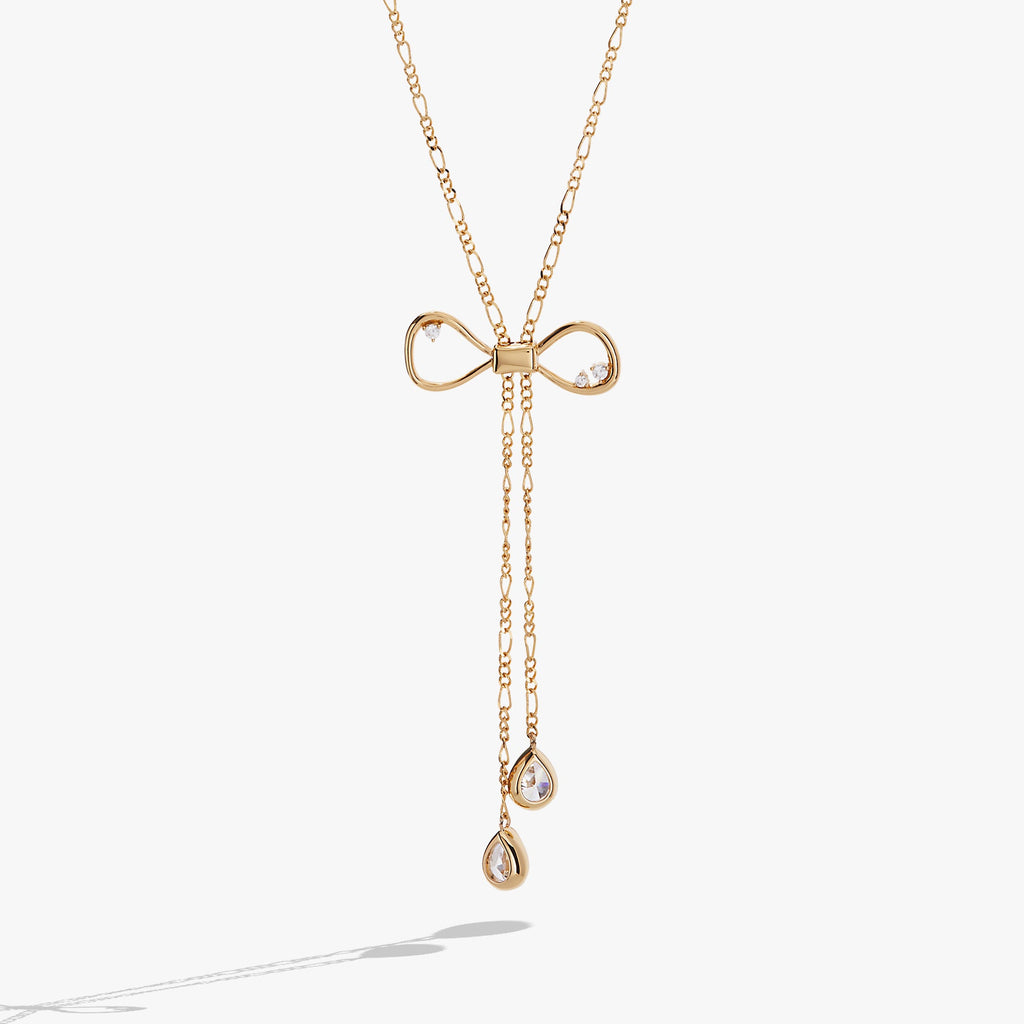 Gold-toned coquette bow necklace featuring clear geometric crystals and an adjustable slider mechanism