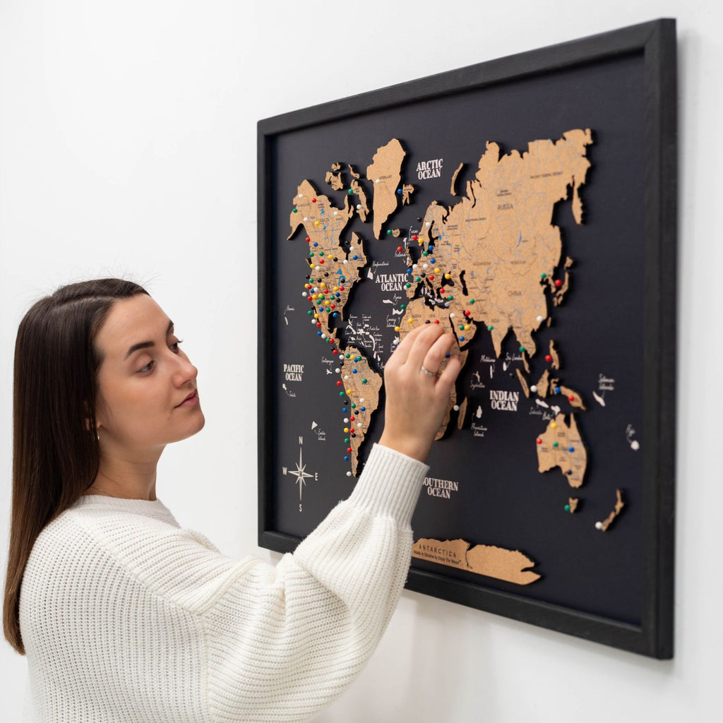 A minimalist brown cork world map with black detailing, mounted on a wall for travel tracking.