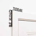 Minimalist black wooden 'Be Kind Today' wall quote installed in a modern room corner.