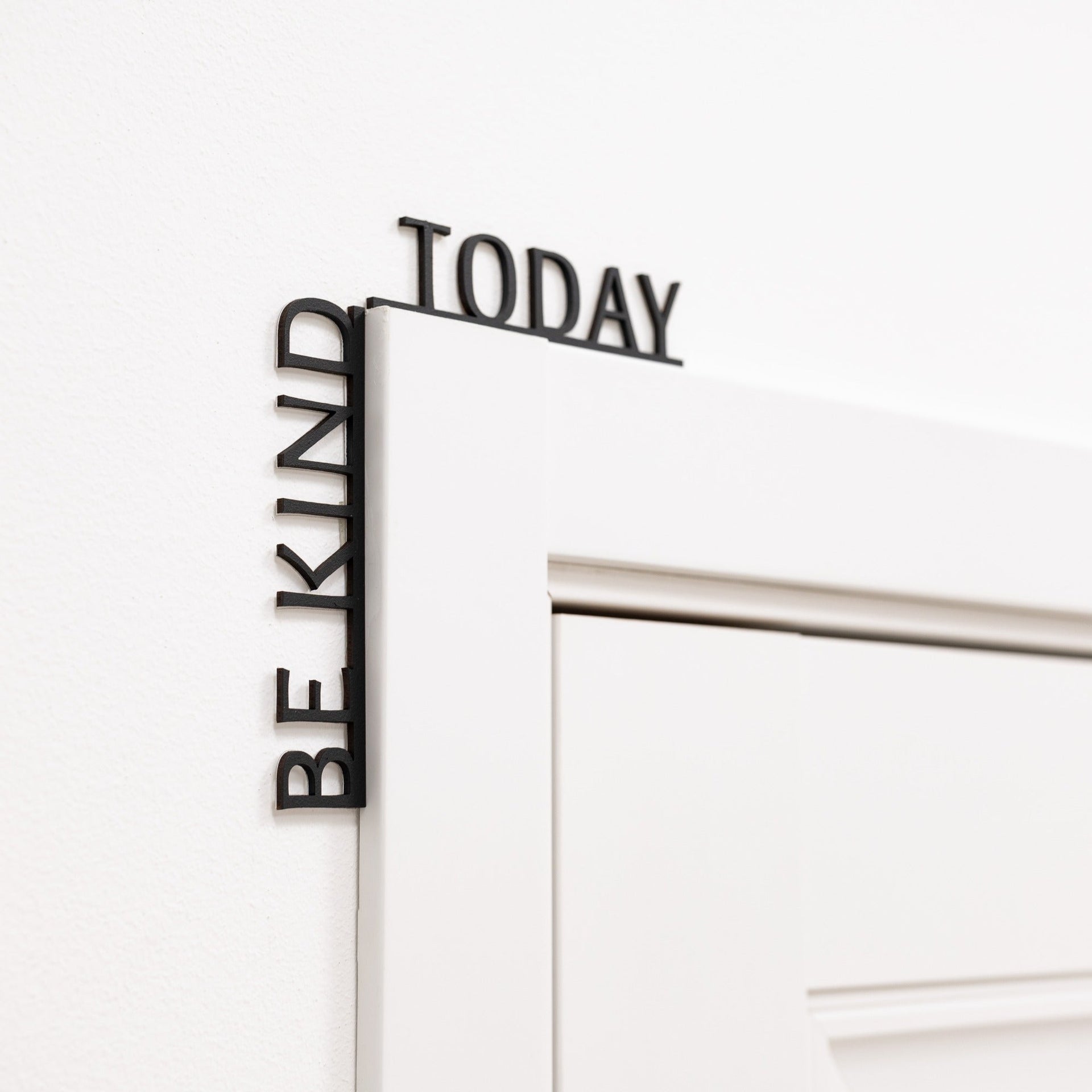Minimalist black wooden 'Be Kind Today' wall quote installed in a modern room corner.