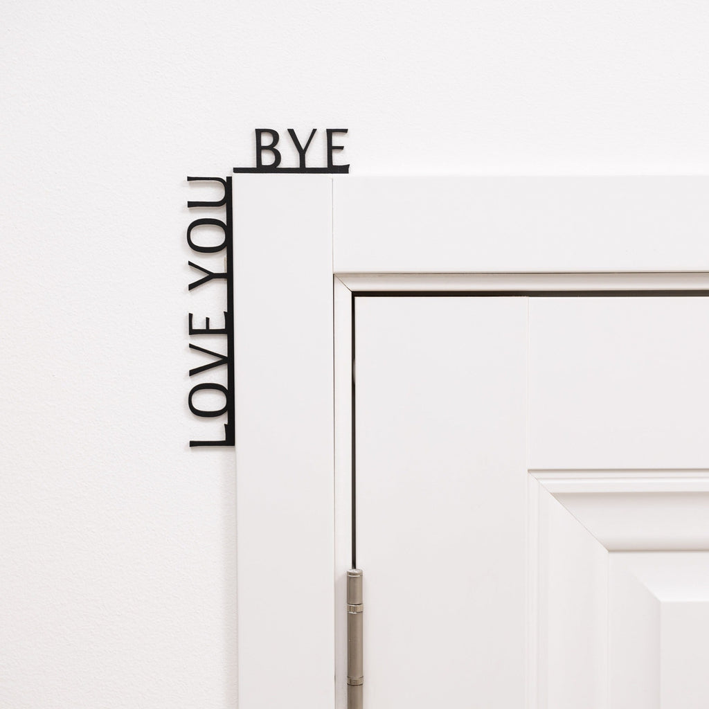 Black minimalist wooden wall art reading Love You Bye, positioned in a corner.