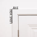Black minimalist wooden wall art reading Love You Bye, positioned in a corner.
