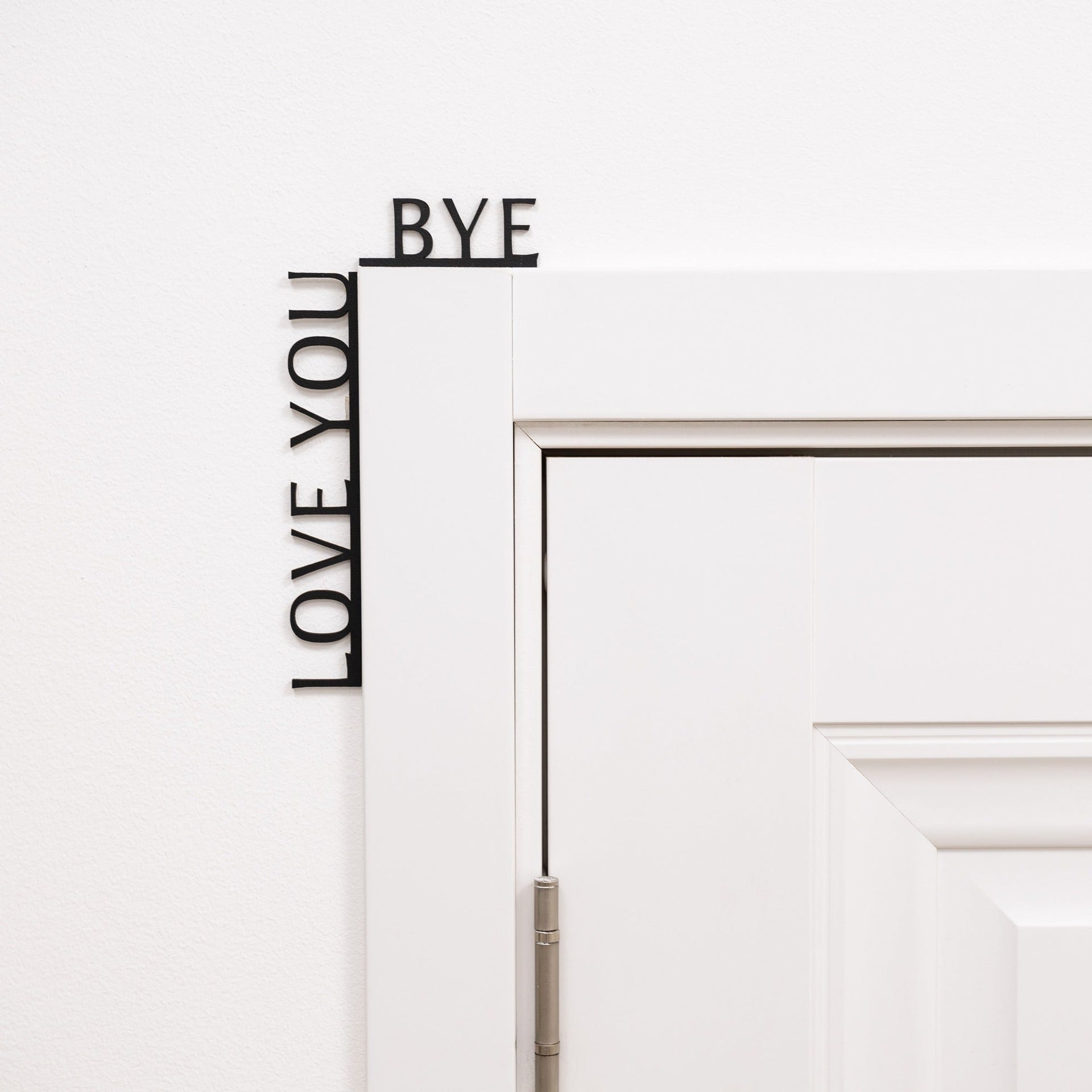 Black minimalist wooden wall art reading Love You Bye, positioned in a corner.