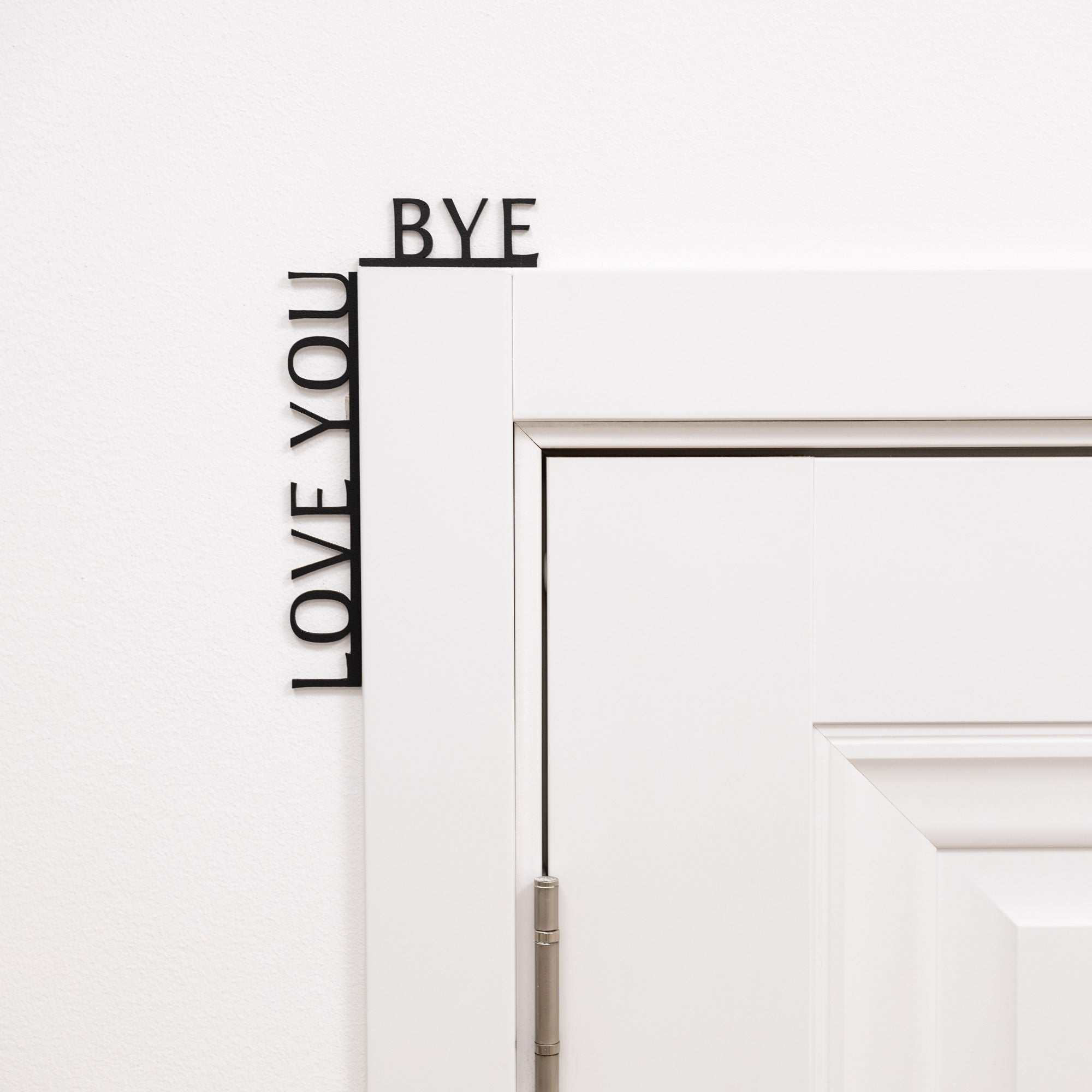 Black minimalist wooden wall art reading Love You Bye, positioned in a corner.