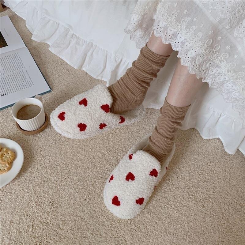 Women's plush white indoor slippers featuring vibrant red heart patterns on a soft fabric texture.