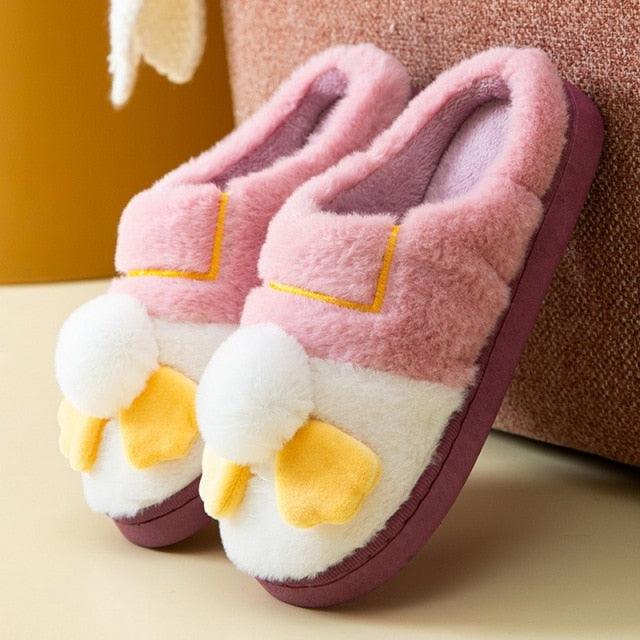 A pair of soft, pastel-colored fuzzy faux fur house slippers on a wooden floor, representing modern casual home loungewear.