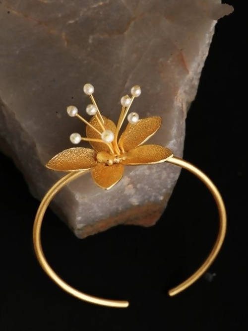Close-up of a women's matt golden flower bracelet with romantic floral patterns and oxidized details.