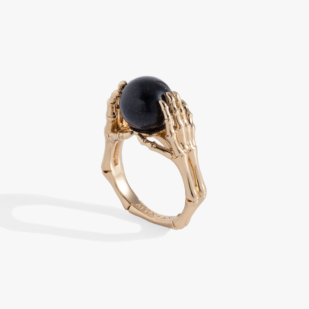 Close-up of a polished silver ring featuring detailed skeleton hands holding a round, deep navy-blue crystal ball.