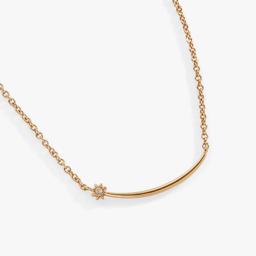 Close-up of a polished gold celestial shooting star necklace with a clear crystal accent worn as a short collar