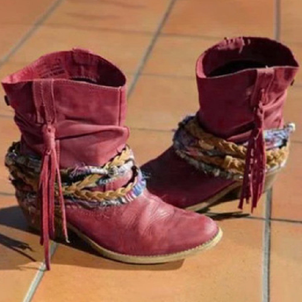 A pair of women's fashion ankle boots in a soft earth tone featuring a decorative braided wrap and tassel fringe detail, shown on a tiled surface.