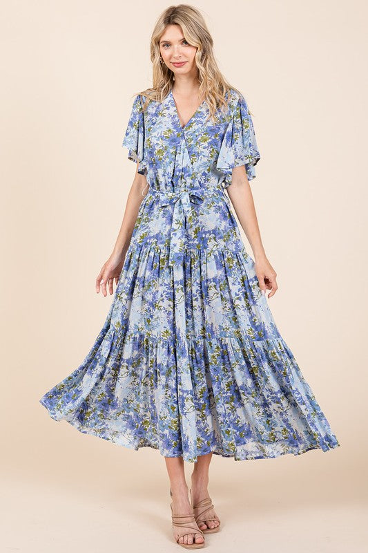 Model wearing a flowy floral tiered flutter sleeve dress with a tie waist