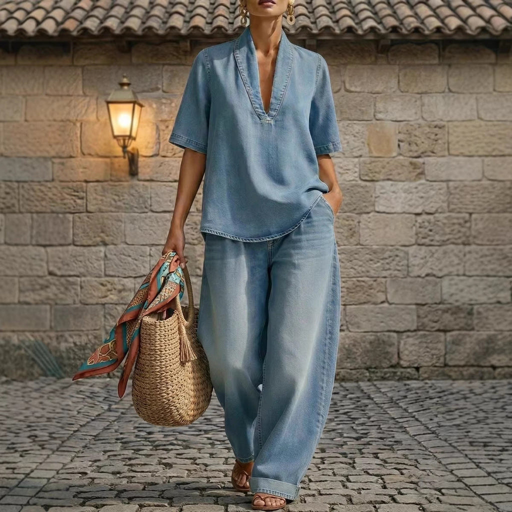 A woman wearing a light-wash denim V-neck top and matching wide-leg jeans in a stone-paved square.
