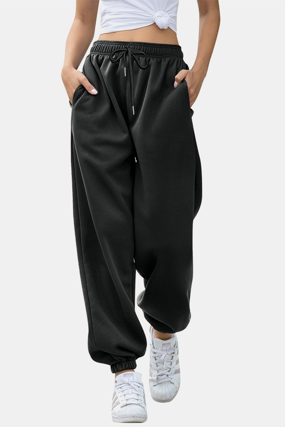 Model wearing black elastic waist joggers with drawstring and side pockets, showing a relaxed fit and cuffed ankles.