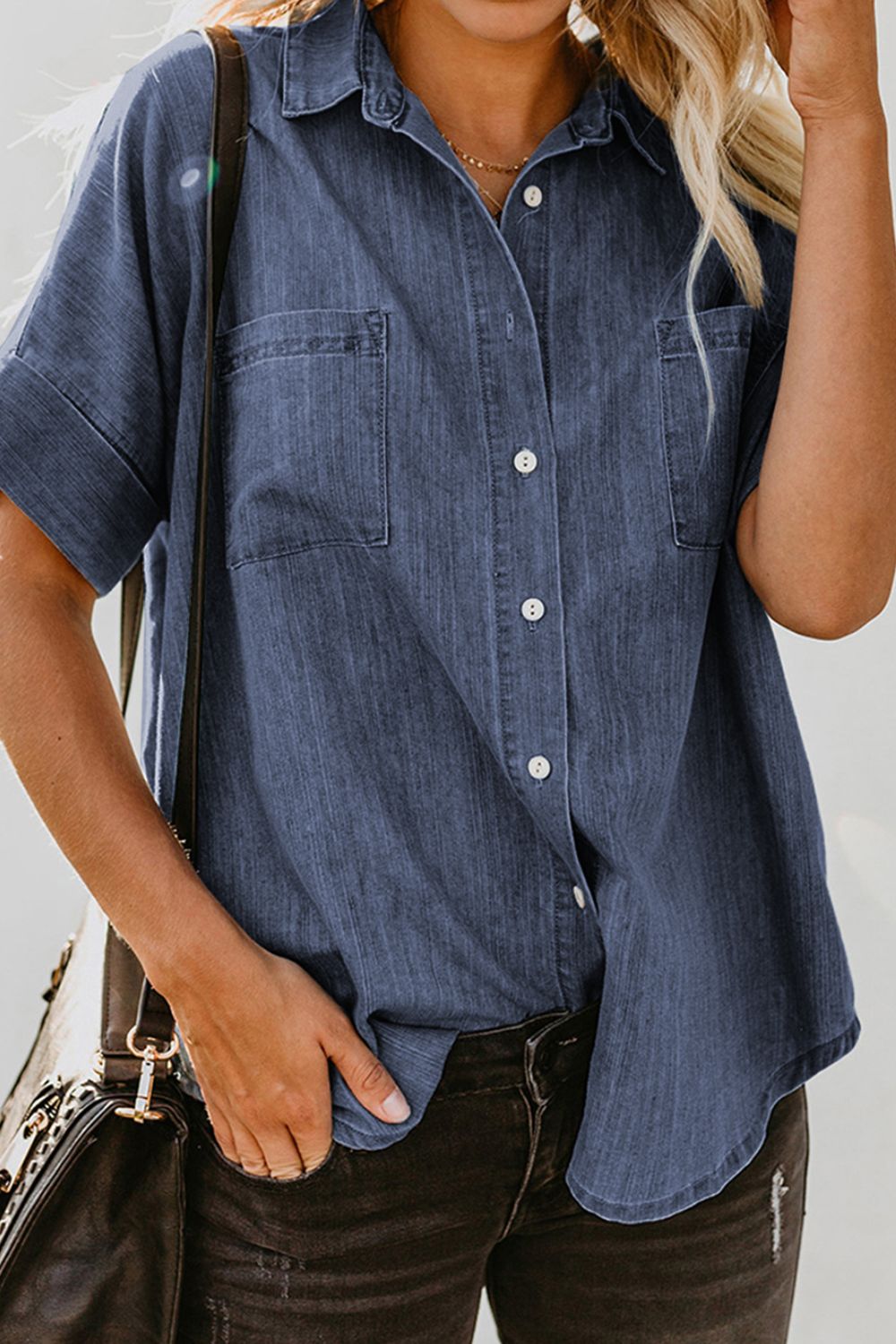 A woman wearing a blue short-sleeve denim button-up shirt with a chest pocket and a curved hem.