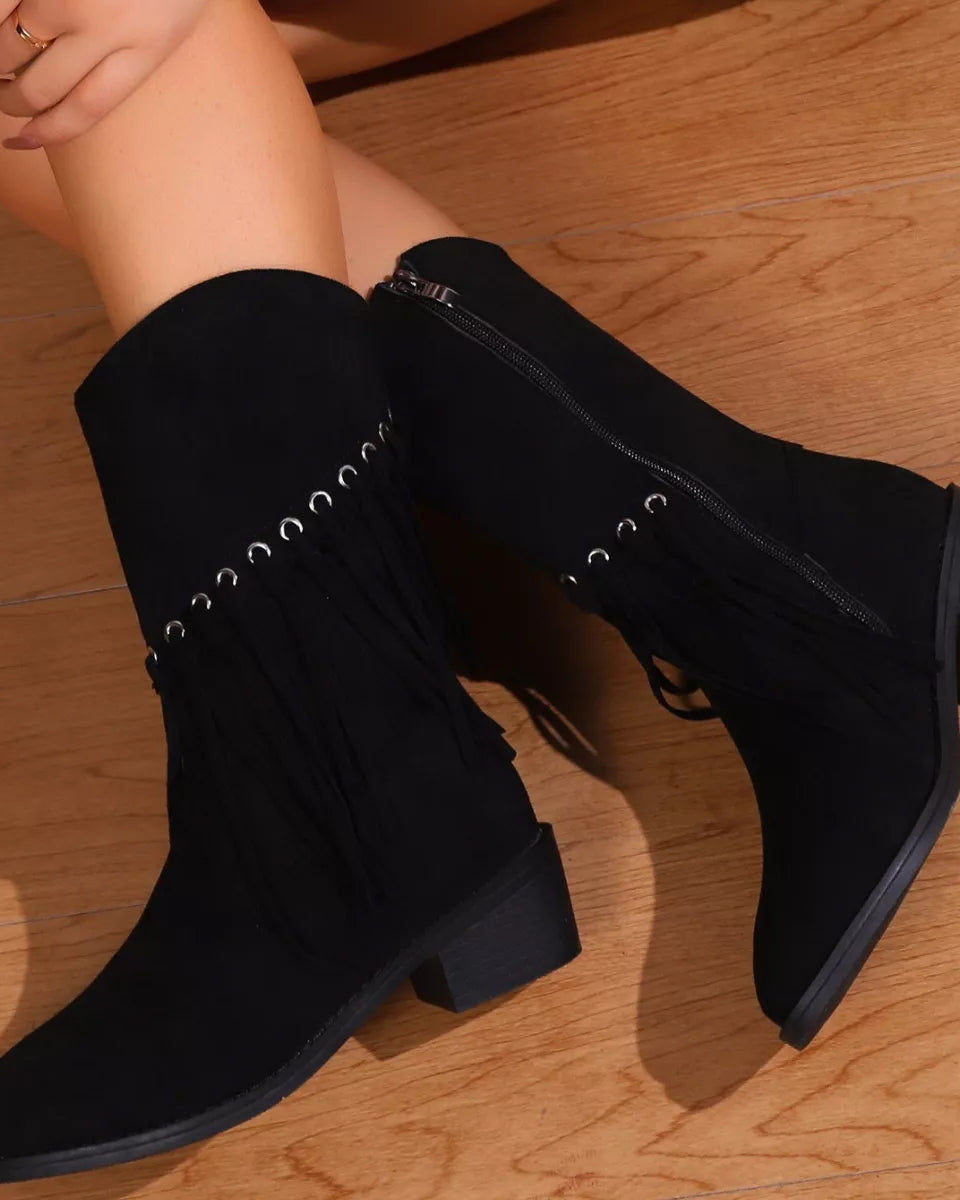 Black knee-high boots with decorative laces on a wooden floor