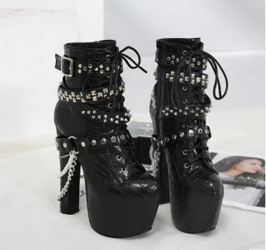 A pair of black platform ankle boots featuring chunky heels, silver studs, and decorative chain accents.