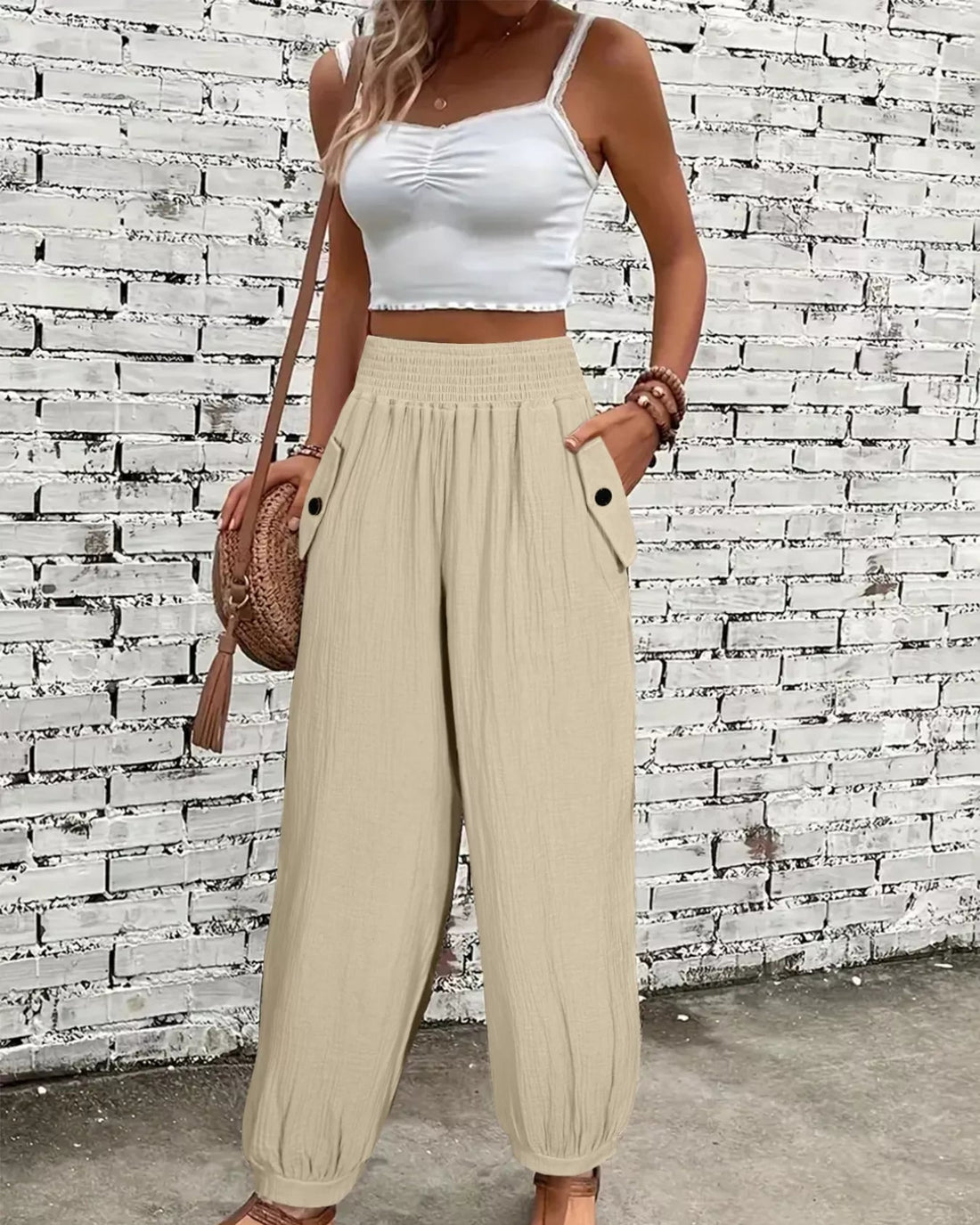 Woman wearing a white top and beige wide-leg pants against a textured wall.