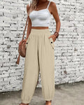 Woman wearing a white top and beige wide-leg pants against a textured wall.