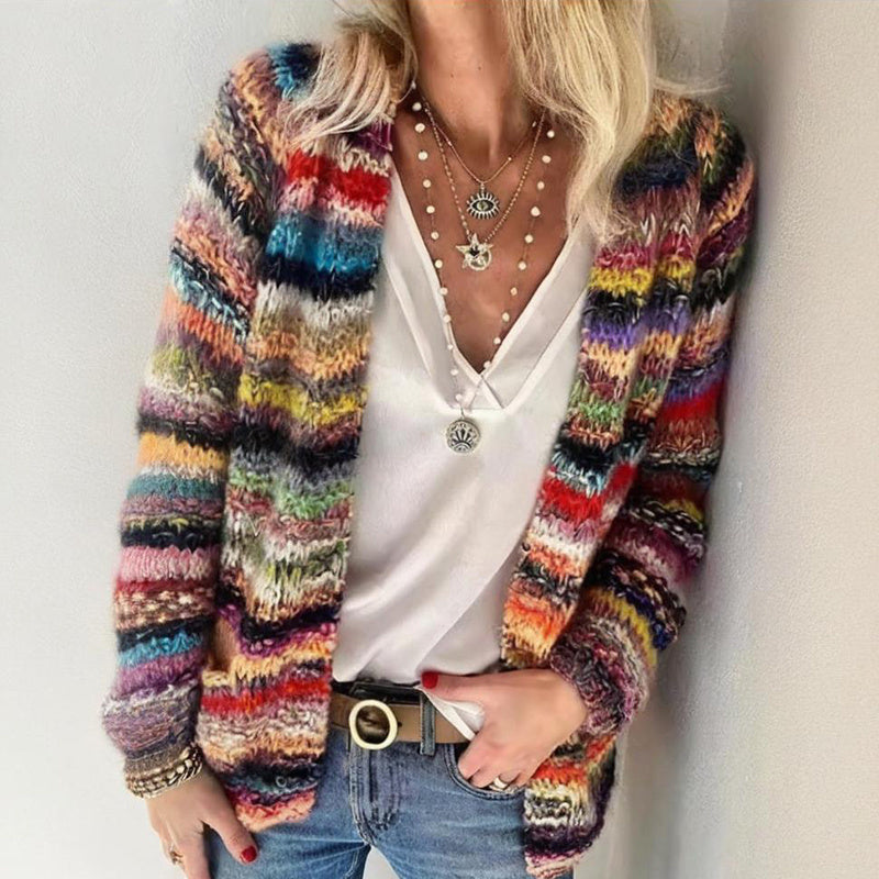 A woman wearing a vibrant multi-colored long sleeve open-front knit cardigan paired with a white tank top and blue jeans.