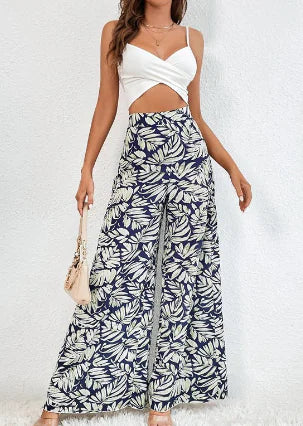 A woman wearing high-waist wide-leg trousers with a tropical leaf print pattern, styled with a white crop top.