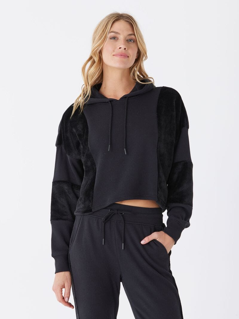 A close-up of a women's black sherpa and fleece pullover hoodie showing the texture and hood detail.