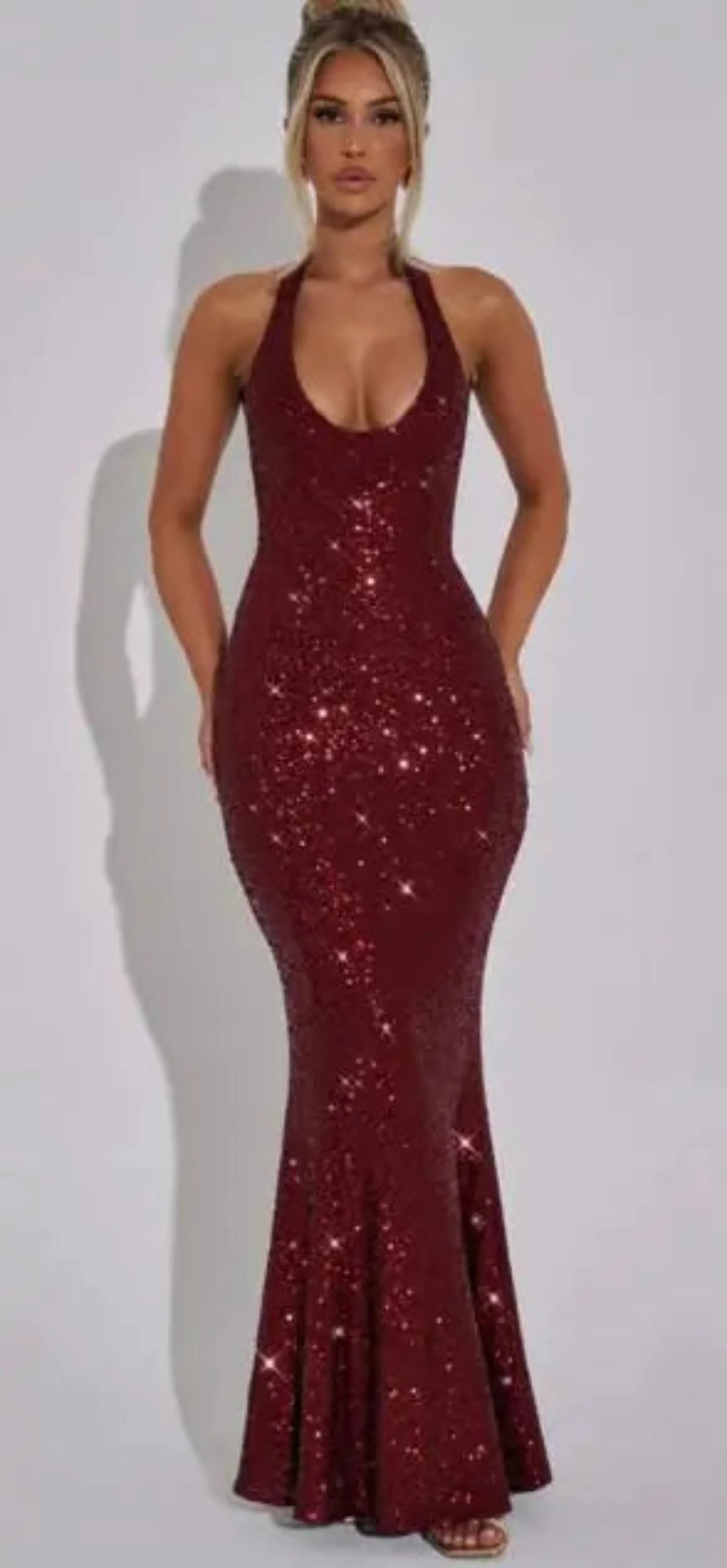 A woman wearing a fitted burgundy sequin halter maxi dress
