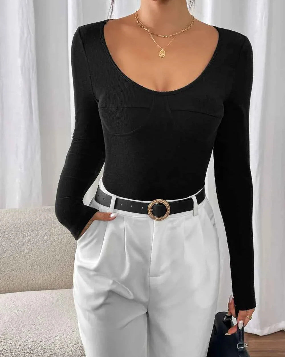 Person wearing a black long-sleeve top and white pants with a blurred background