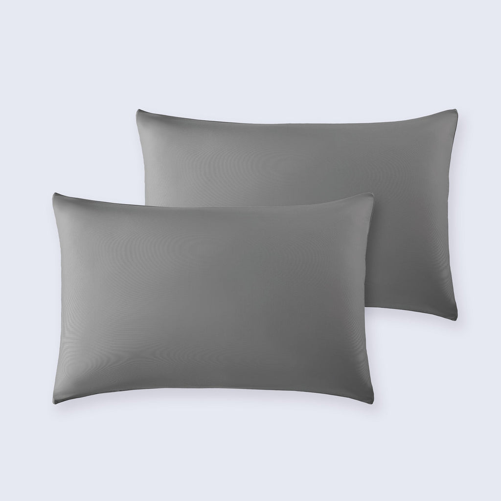 Set of two gray cooling pillowcases resting on a white bed sheet