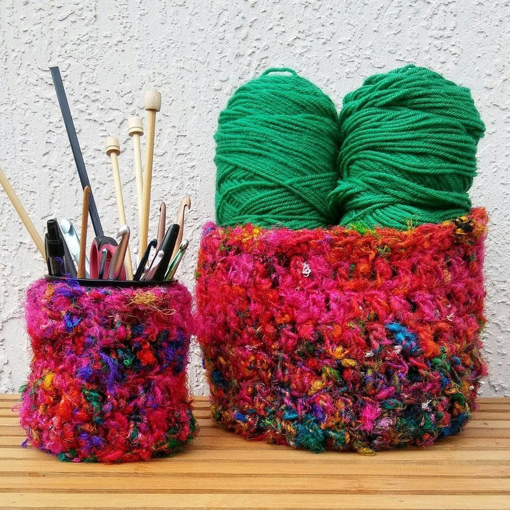 Bohemian-style handmade crochet basket in vibrant pink, orange, and teal multi-tonal silk yarn sitting on a wooden surface.