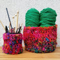 Bohemian-style handmade crochet basket in vibrant pink, orange, and teal multi-tonal silk yarn sitting on a wooden surface.