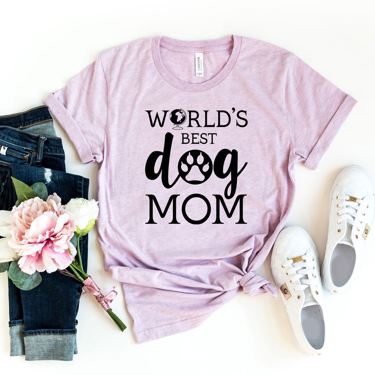 A lavender short-sleeve t-shirt with 'World's Best Dog Mom' printed in black text, styled on a white background with jeans and sneakers.