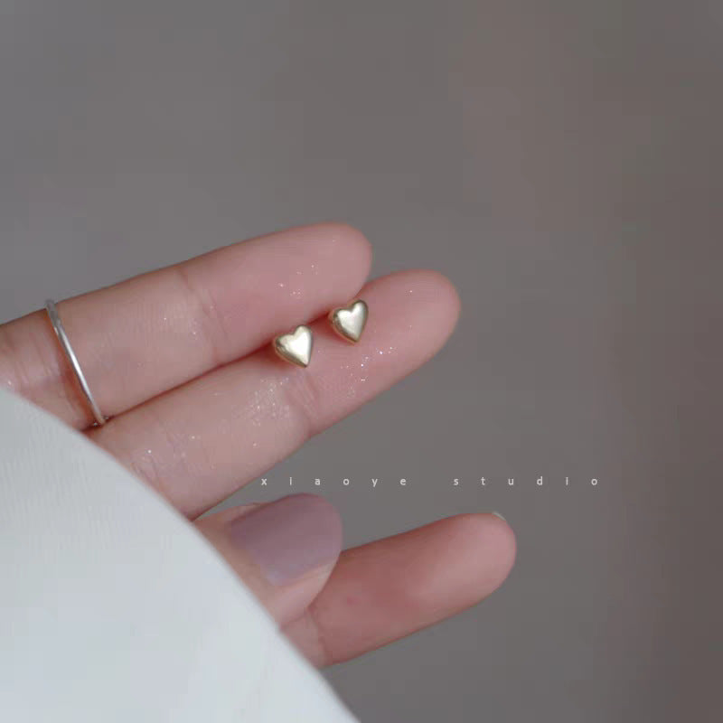Minimalist gold-plated heart stud earrings on a neutral background