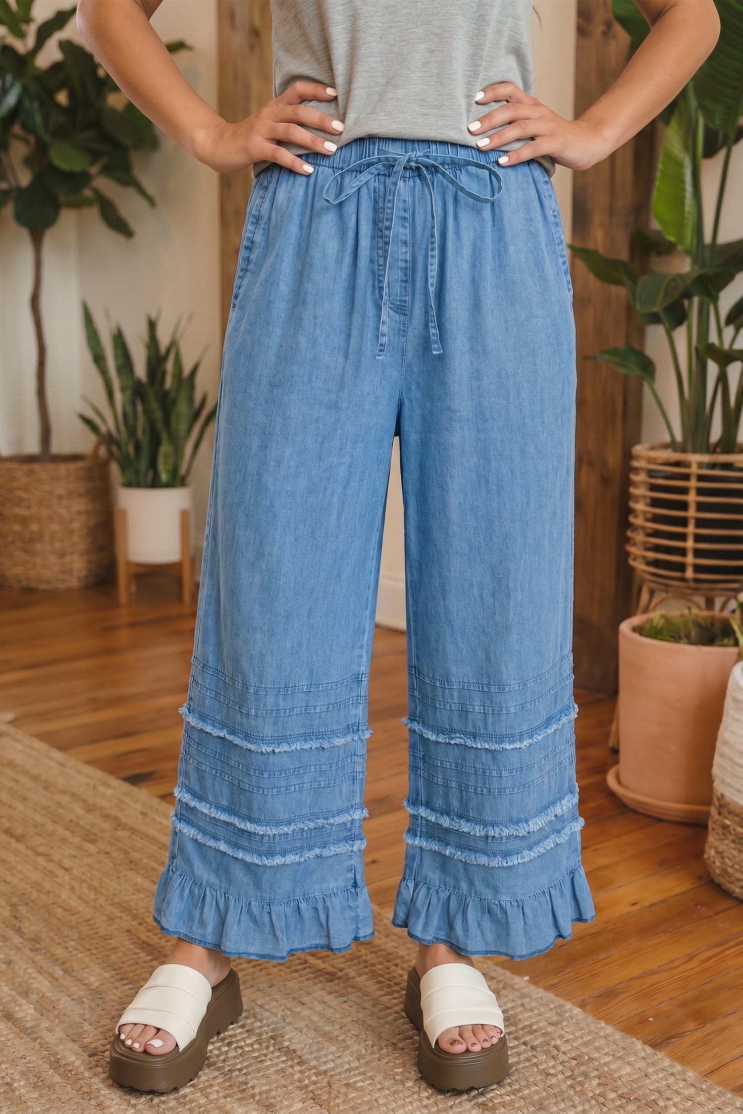 A pair of light blue chambray wide leg pants with a ruffled hem, styled in a relaxed bohemian look.