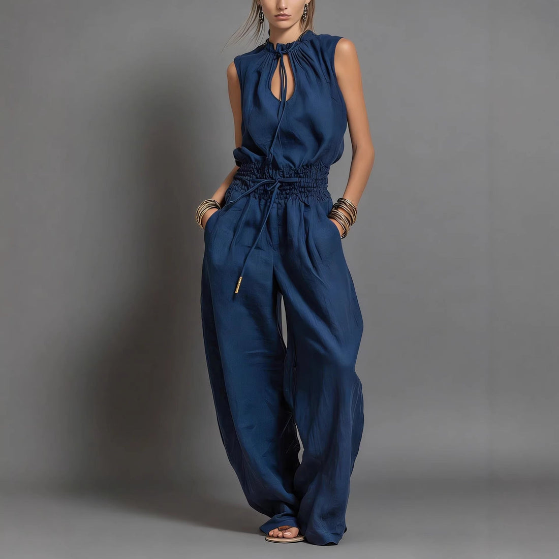 Model wearing a navy blue sleeveless high-waist wide-leg jumpsuit with a tie-waist detail on a city street.
