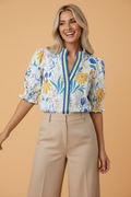 Woman wearing a floral V-neck blouse with puff sleeves and stripe trim details in white, blue, yellow, and orange.