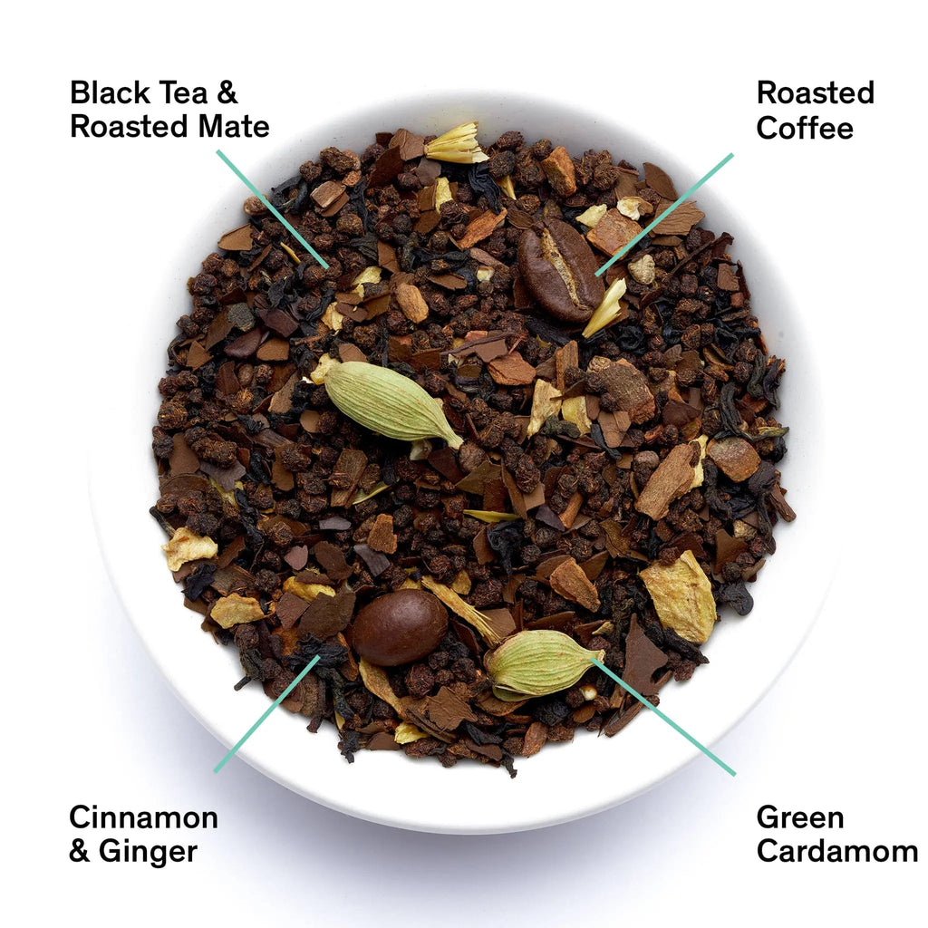 A close-up overhead view of loose leaf Dirty Chai tea, featuring visible whole coffee beans, green cardamom pods, black tea leaves, ginger, and roasted mate.