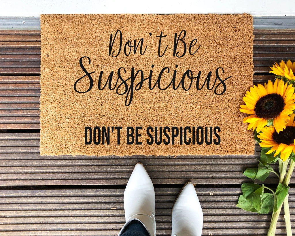 A brown coir doormat with black printed text that reads Don't Be Suspicious.