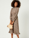 Woman wearing a brown and green floral midi dress with puff sleeves and smocked neckline.