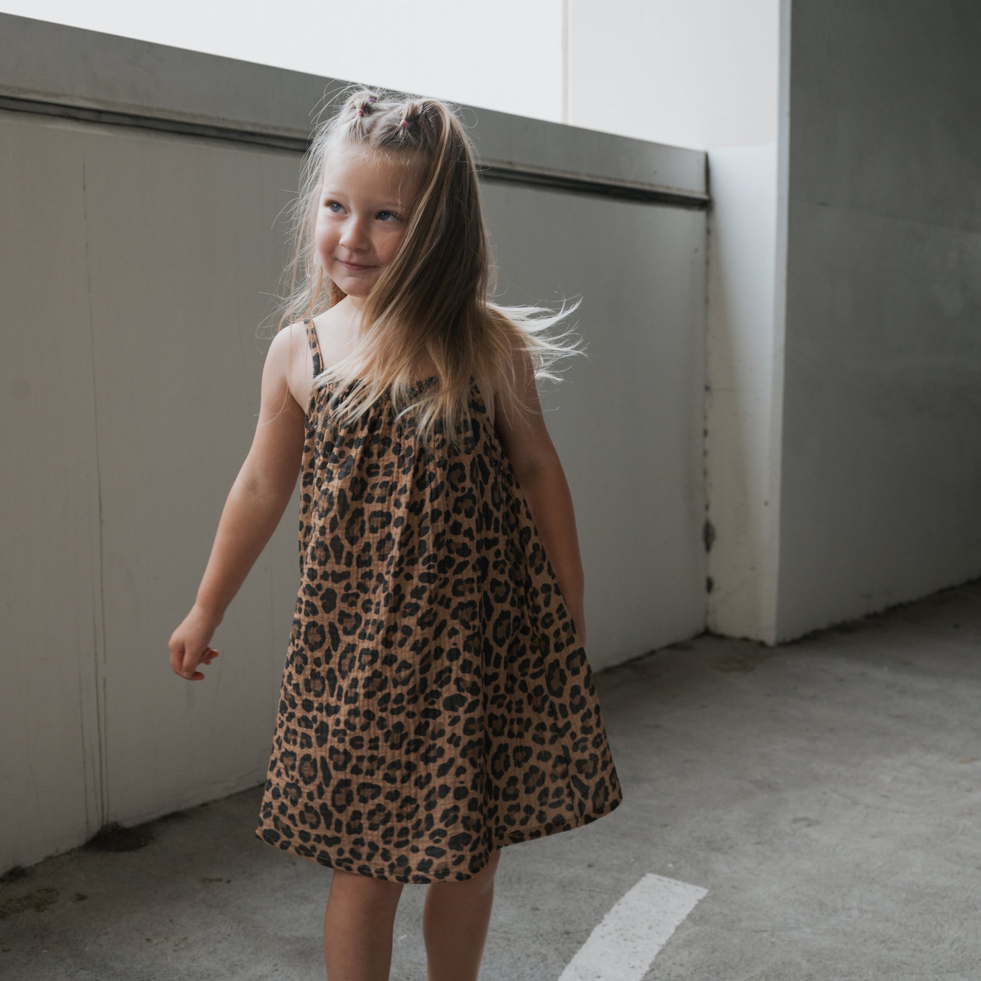 A child wearing a sleeveless, knee-length leopard print muslin dress in a bohemian casual style.