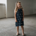 Girl wearing navy blue Emery knit dress with white pom-poms and adjustable tie straps