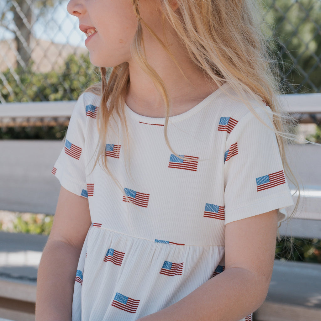 A girl wearing a casual, patriotic red, white, and blue flag print ribbed bamboo t-shirt dress with a relaxed fit.