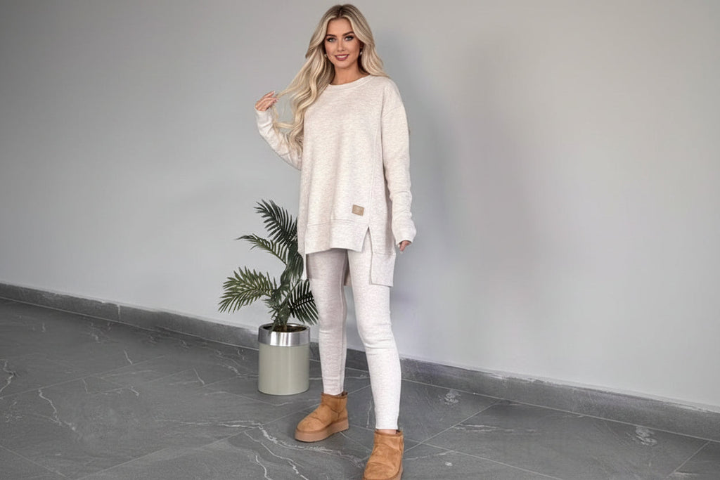 A woman wearing a beige 2-piece lounge set consisting of an oversized sweatshirt with side slits and matching high-waisted leggings.
