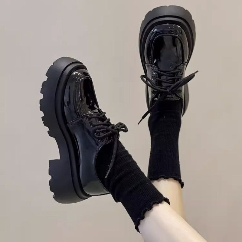 Close up of woman wearing shiny black British style chunky platform loafers with black socks.