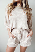Woman wearing a beige and cream knit loungewear set with a bracelet sleeve cropped top and drawstring shorts.