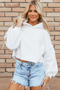 A woman wearing a white sherpa fleece drop shoulder hoodie with exposed seams, viewed from the front and back against a brick wall.